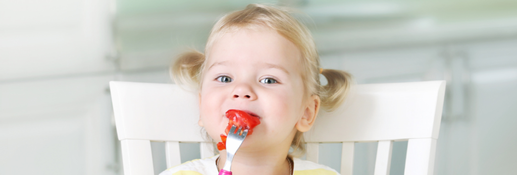 menina pequena comendo um tomate com um garfo