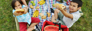 mesa de piquenique com frutas e crianças segurando pães