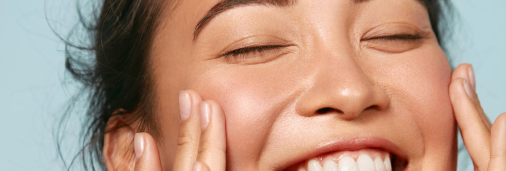 Uma mulher de pele clara sorrindo e mostrando uma pele saudável do rosto